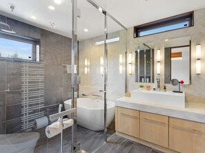 A modern bathroom with a glass shower enclosure, a freestanding bathtub, and a vanity with a large mirror.