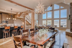 A spacious kitchen with a wooden staircase, a dining area with a large wooden table, and a view of the mountains through large windows. - Lodge-style home with striking mountain views, fireplaces, & hot tub (South Fork)