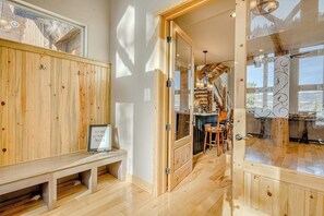A wooden interior with a bench, a glass door, and a staircase leading to a balcony. - Lodge-style home with striking mountain views, fireplaces, & hot tub (South Fork)