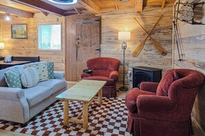 Ein gemütliches Blockhaus-Interieur mit Sofa, Sesseln, einem Tisch, einem Kamin und Holzwänden.