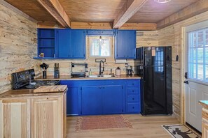 Eine Küche mit Holzwänden, blauen Schränken, einem schwarzen Kühlschrank und einem Fenster mit Jalousien.