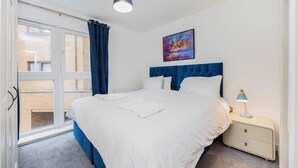 Un dormitorio con una cama grande, una mesita de noche con lámpara, una ventana con cortinas y un cuadro en la pared.
