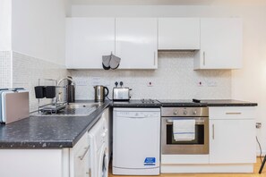 A compact kitchen with white cabinets, a dishwasher, an oven, a toaster, and a kettle. - Charming Apartment for Friends, Couples and Families in London - Hackney 3 (London)