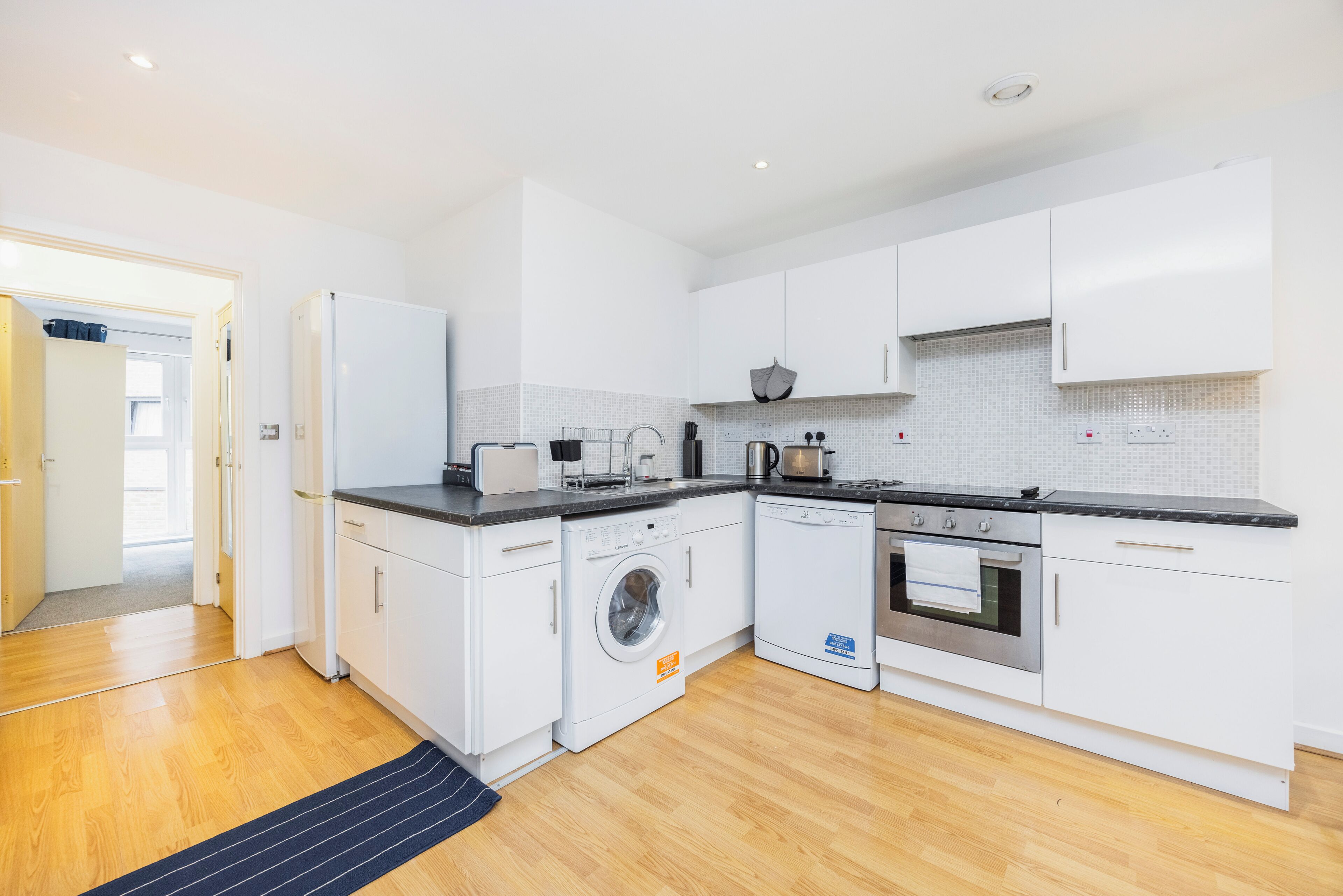 A modern kitchen with white cabinets, a washing machine, an oven, and a dishwasher.