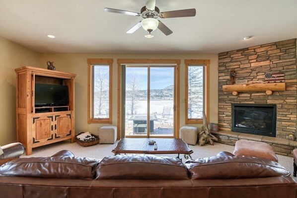 A living room with a stone fireplace, a television, a wooden cabinet, and a leather couch. - Dog-Friendly Golf Course Front Home w/Free WiFi, Gas Fireplace, W/D, & Gas Grill (South Fork)