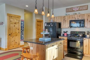 A kitchen with wooden cabinets, a black refrigerator, a stove, and a microwave. There is a welcome sign on the door and a 'Home Sweet Home' sign above the cabinets. - Dog-Friendly Golf Course Front Home w/Free WiFi, Gas Fireplace, W/D, & Gas Grill (South Fork)