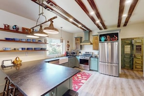 A modern kitchen with a large island, stainless steel appliances, and wooden beams on the ceiling. - Mountain view modern home with open layout, gas fireplace, smart TVs, & W/D (South Fork)