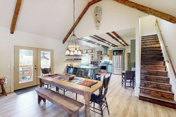 A spacious kitchen with wooden beams, a dining area with a wooden table, and a staircase. - Mountain view modern home with open layout, gas fireplace, smart TVs, & W/D (South Fork)