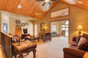 A spacious living room with a high ceiling, wooden beams, a fireplace, a television, and a large window. - Inviting Condo Near Town w/ Jetted Tub, Full Kitchen, Balcony & Free WiFi (South Fork)