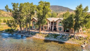 Une maison à deux étages avec une façade en pierre, un porche à l’avant et une rivière au premier plan.