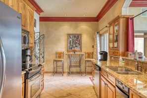 A kitchen with wooden cabinets, a granite countertop, a stainless steel refrigerator, and a dining area with two chairs. - Inviting Condo Near Town w/ Jetted Tub, Full Kitchen, Balcony & Free WiFi (South Fork)