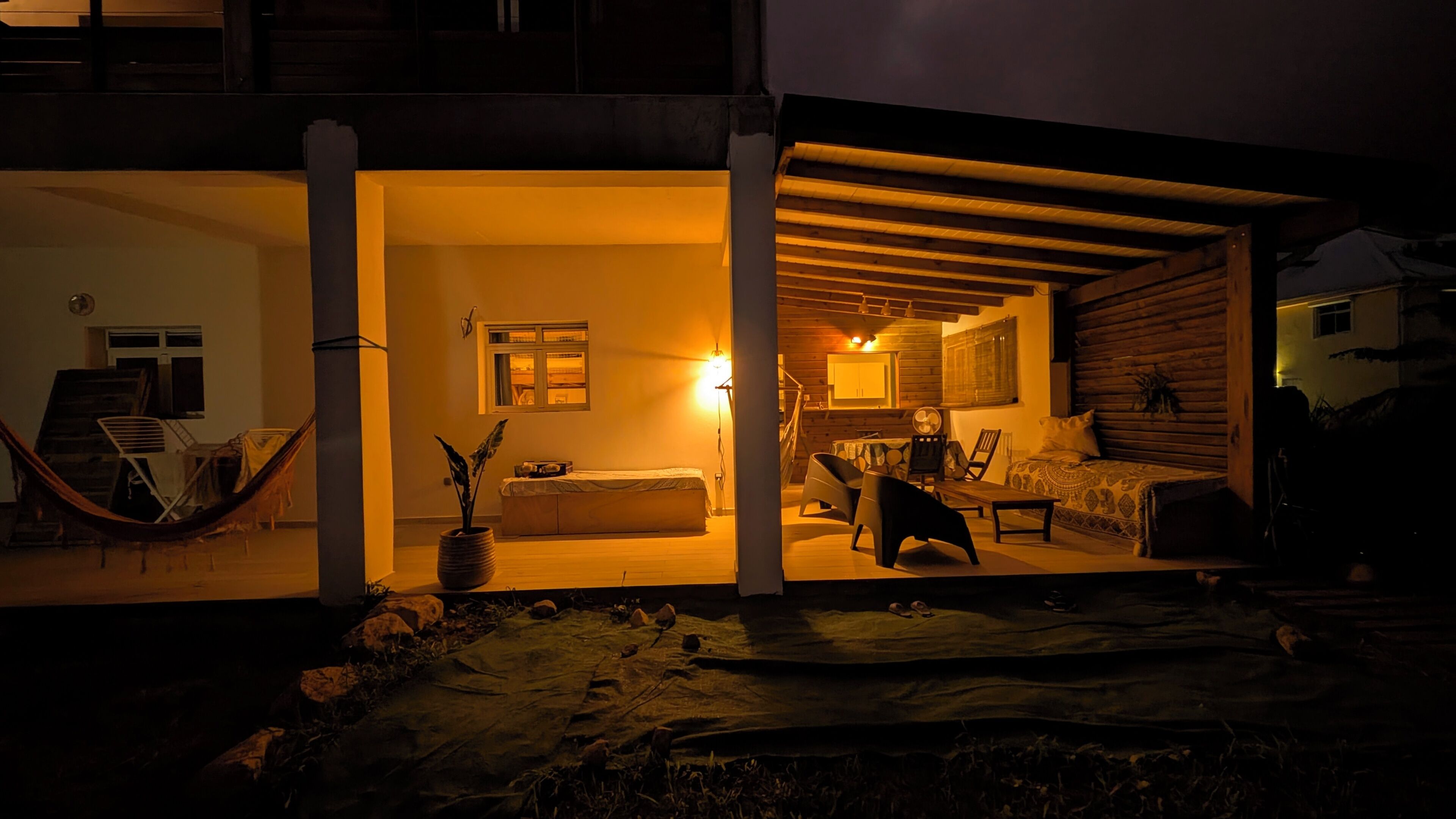 Ein modernes Haus mit überdachter Terrasse, einer Hängematte, einem Blumentopf und einem Bett.