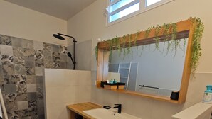 Een badkamer met een douche, wastafel, spiegel en raam.