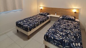 Een slaapkamer met twee eenpersoonsbedden, een plafondventilator, een airconditioning en een raam met gordijn.