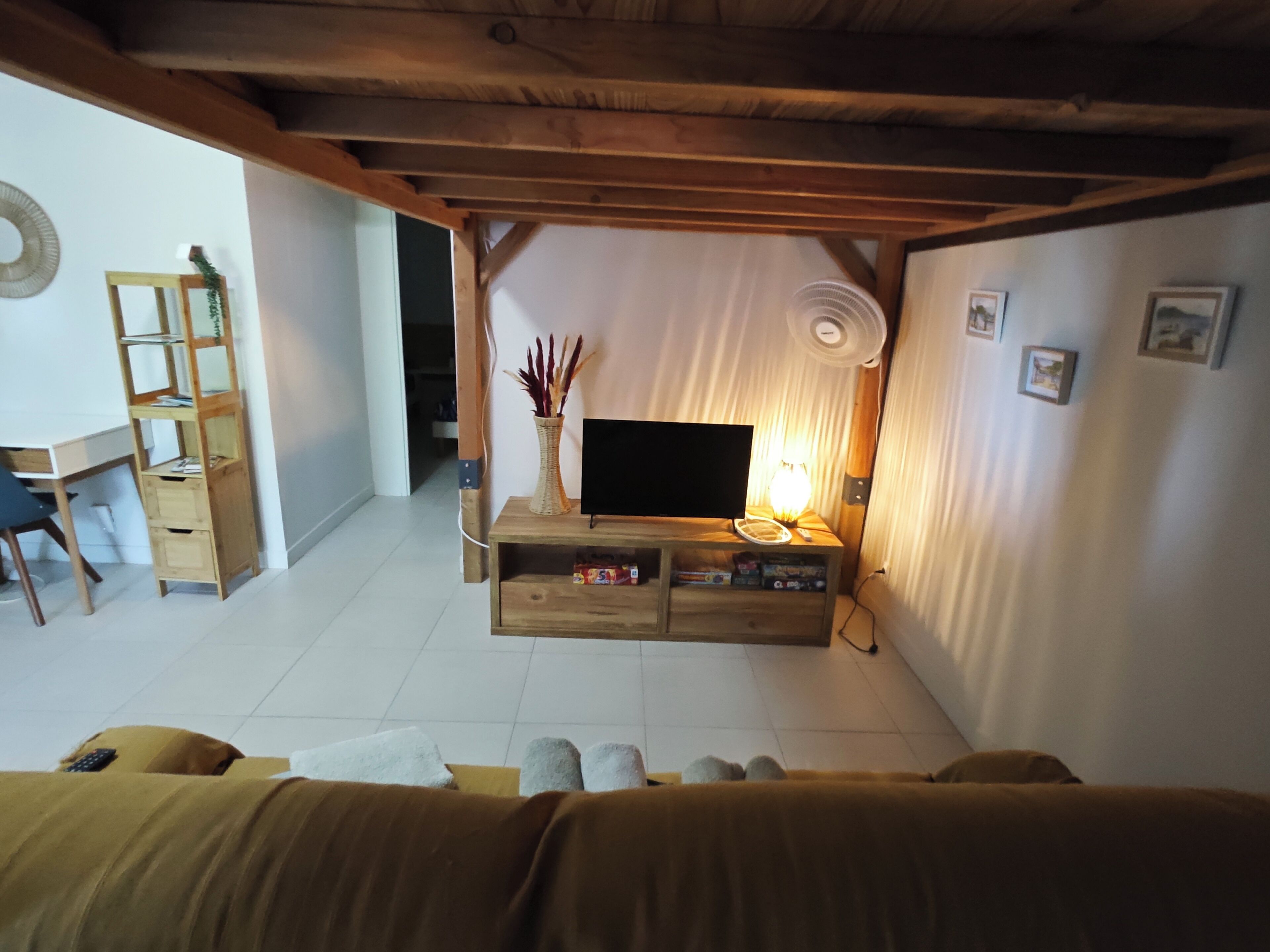 A living room with a TV, wooden furniture, a bookshelf, and a small table with a lamp.