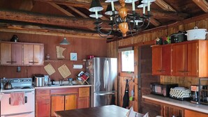 Eine rustikale Küche mit Holzbalken, einem großen Esstisch aus Holz und modernen Geräten.