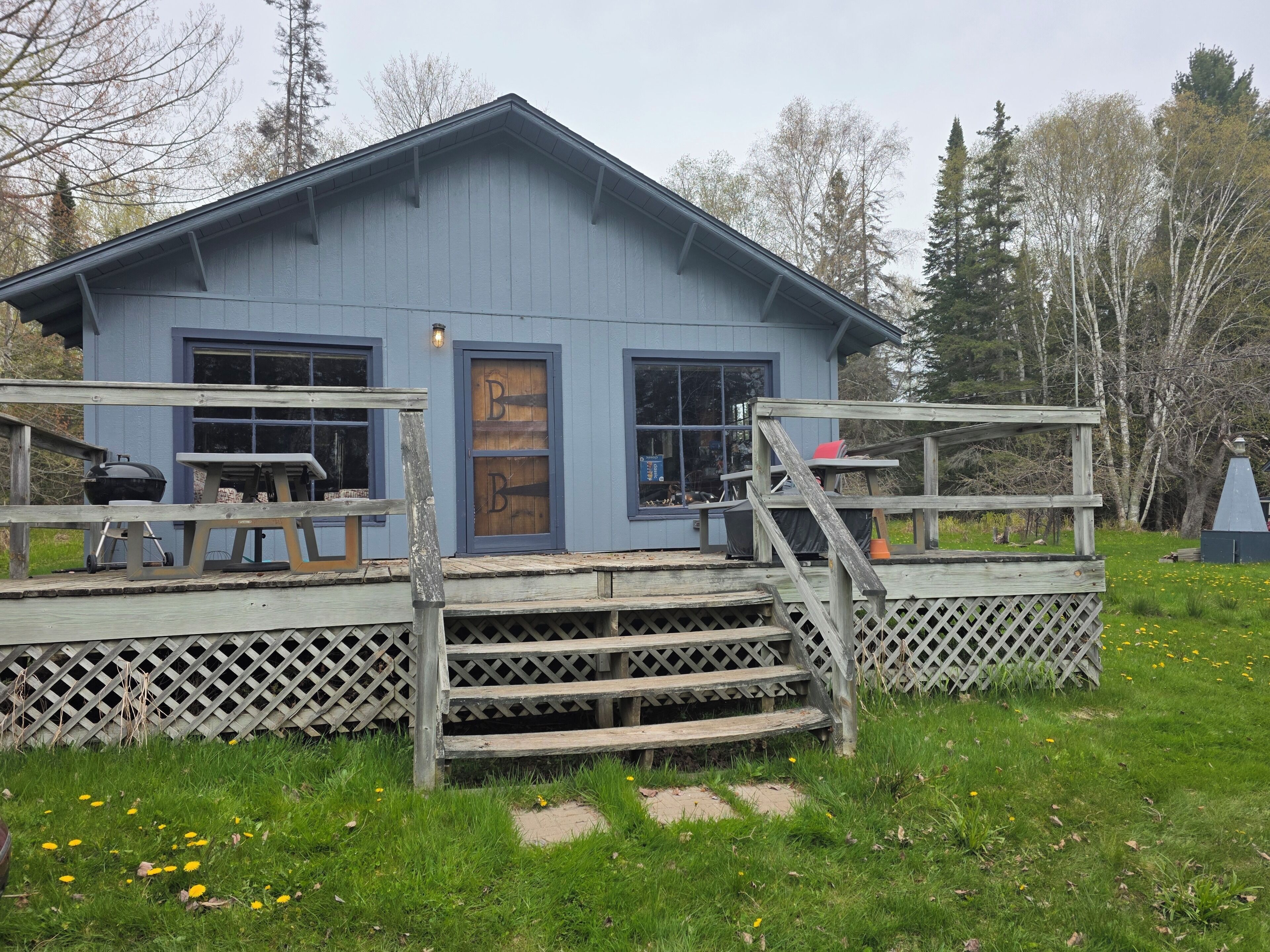 Un petit bâtiment bleu avec une terrasse en bois, un barbecue et un banc.