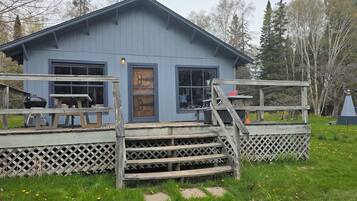 Un petit bâtiment bleu avec une terrasse en bois, un barbecue et un banc.