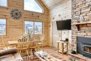 Ein Holzinterieur mit Kamin, einem an der Wand montierten Fernseher und einem Essbereich mit Stühlen und Tisch.