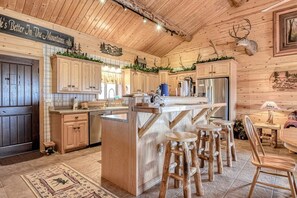 A rustic cabin interior with wooden walls, a kitchen island with stools, and a mounted deer head. - Remodeled, Dog-Friendly Cabin w/ Large Fenced Yard, WiFi & W/D - Great for ATVs (South Fork)