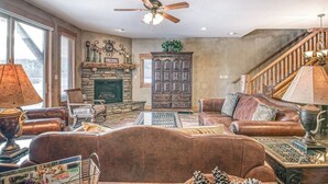 A living room with leather sofas, a fireplace, a wooden cabinet, and a ceiling fan.