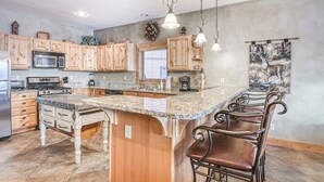 A kitchen with wooden cabinets, a granite countertop, a built-in island with bar stools, and pendant lighting.