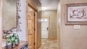A hallway with a wooden door, a framed picture on the wall, and a decorative metal piece on the left.