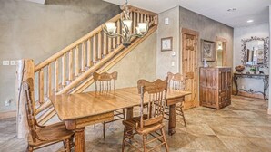 A dining area with a wooden table and chairs, a wooden staircase, and a chandelier.
