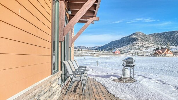 A wooden deck with outdoor seating, a barbecue grill, and a view of snow-covered hills.