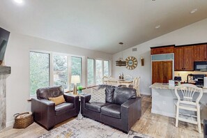 Eine moderne Küche mit Holzschränken, ein Essbereich mit Tisch und Stühlen sowie ein Wohnzimmer mit Ledersofa und Teppich.