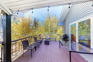 Eine überdachte Terrasse mit Gartenmöbeln, einem Grill und Blick auf Bäume mit gelben Blättern.