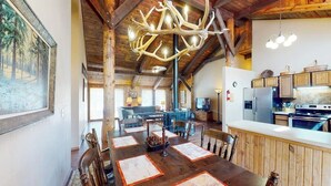 Un coin repas rustique avec une table en bois, des chaises et un grand lustre orné de bois de cerf.
