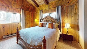 Une chambre aux murs lambrissés, avec un grand lit, deux lampes de chevet et une fenêtre avec des rideaux.