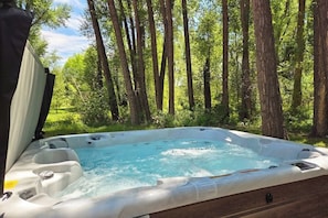 A hot tub in a forested area with trees and greenery in the background. - Rustic home with mountain views, wood stove, hot tub, deck, washer/dryer (South Fork)