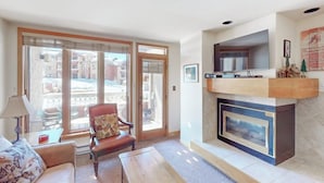 A living room with a fireplace, a sofa, a chair, and a table. - Comfy mountain condo with A/C in every room, pool, hot tub & W/D (Steamboat Springs)