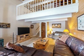 A spacious living area with a high ceiling, a balcony, a television, a sofa, and a coffee table. - Beautiful condo near the lifts with pool, WiFi, private washer/dryer (Steamboat Springs)