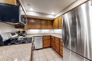 A compact kitchen with a stainless steel refrigerator, a microwave, a stove, and wooden cabinets. - Beautiful condo near the lifts with pool, WiFi, private washer/dryer (Steamboat Springs)