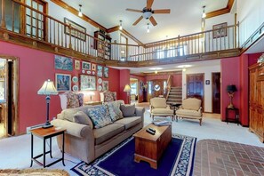 A spacious living room with a high ceiling, a staircase, and a balcony. - Posh mansion with antique decor, WiFi, & gas fireplace - near river and skiing (South Fork)