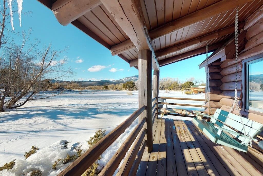 Une cabane en bois avec un porche, un banc et une vue sur un paysage enneigé.