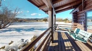 A wooden cabin with a porch, a bench, and a view of a snowy landscape.