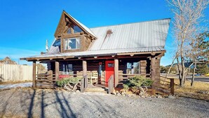 A rustic log cabin with a metal roof, a porch, and a red door.