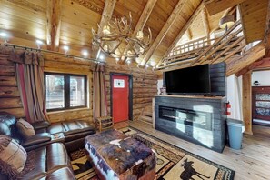 Interior de una cabaña de troncos con un sofá de cuero, chimenea, televisor y candelabro.