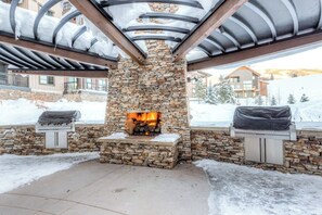 Ein Steinkamin mit Feuer, umgeben von einer überdachten Terrasse mit Steinwänden und Metallstreben.