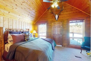 Ein Schlafzimmer einer Holzhütte mit einem Bett, einem Deckenventilator, einem aufgehängten Hirschschädel und Blick ins Freie.