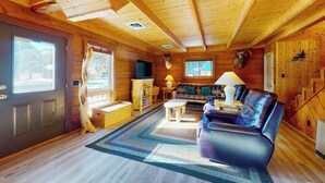 A log cabin interior with a wooden ceiling, a sofa, a television, and a fireplace. - Riverfront home with river & valley views, wood stove, deck, & W/D (South Fork)