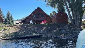 A cabin with a deck, two Adirondack chairs, and a shed by a river. - Riverfront home with river & valley views, wood stove, deck, & W/D (South Fork)
