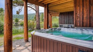 Un bain à remous sous une pergola en bois, avec vue sur les arbres et les collines.