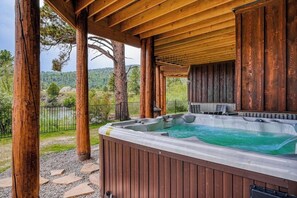 Un jacuzzi bajo una pérgola de madera con vistas a árboles y colinas.