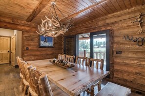 Un intérieur en bois avec une table à manger, des chaises, un lustre et une vue par une fenêtre.