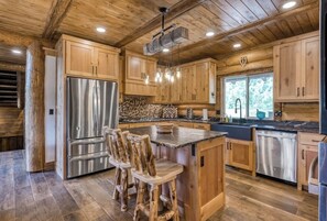 Una cocina con armarios de madera, un refrigerador de acero inoxidable, encimera de granito y una isla de madera con taburetes de bar.